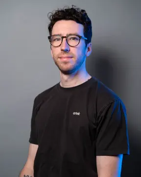 Studio portrait of Jordan Burgess wearing glasses.